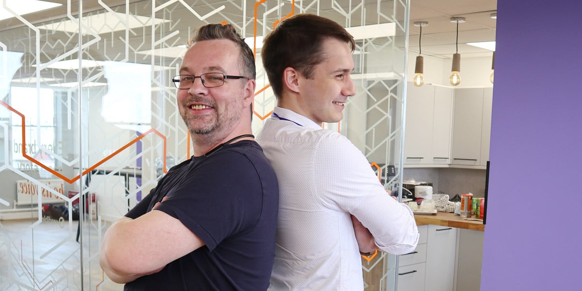 two men smiling and standing back to back symbolizing mutual benefit, help, and support you get from cause marketing campaignsl